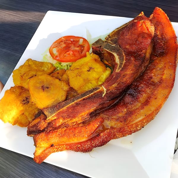 Crispy fried pork chop with tostones, lettuce, and tomato on a white plate.