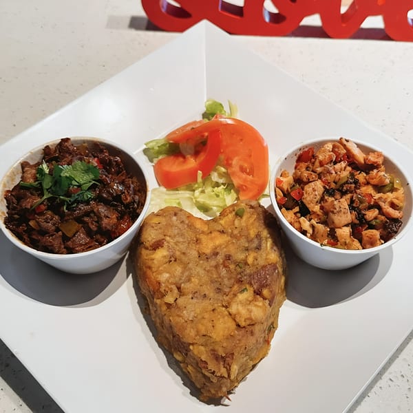 A heart-shaped mofongo with two sides of meat and a small salad on a white plate.