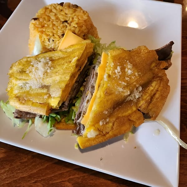 A Puerto Rican mofongo sandwich with cheese and meat, served with yellow rice on a white plate.